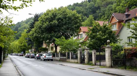 Családi házas utca kerítésekkel, háttérben erdős domboldal